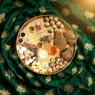Brass plate of Viha pooja samagri (pooja items) with cowrie shells, seeds and kumkum (red powder) on green silk