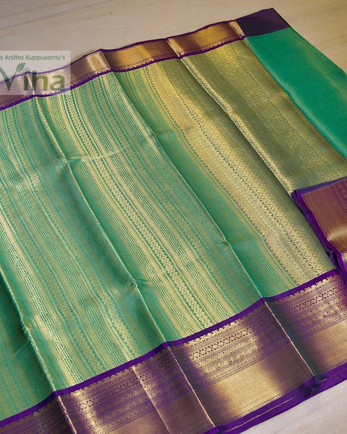 Premium Katan Silk Saree With Blouse, a folded green textile featuring shiny gold-toned patterned stripes and purple borders