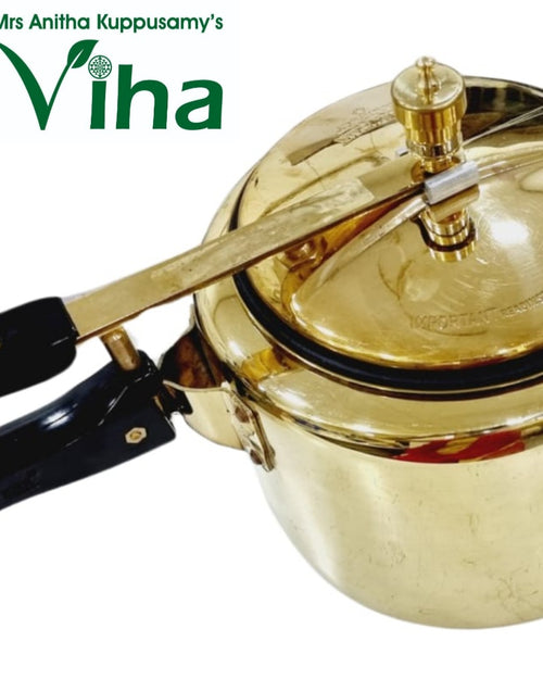 Brass-toned pressure cooker with black handles and a gold pressure valve