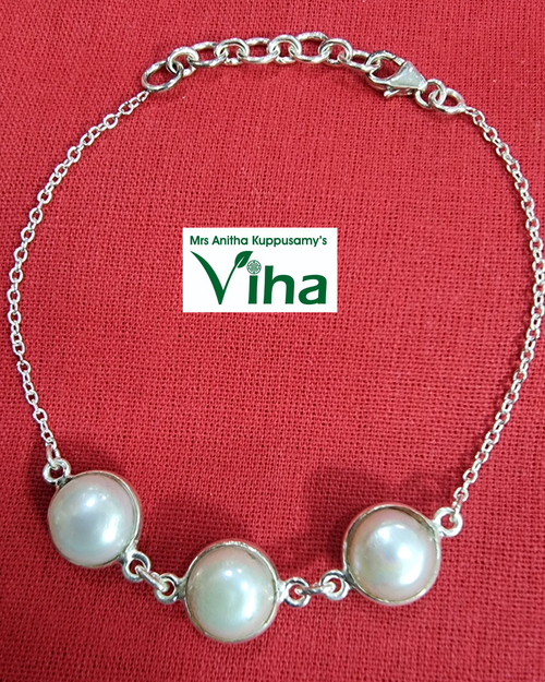 Pearl Bracelet Silver chain with three round pearl beads, laid on a red fabric background