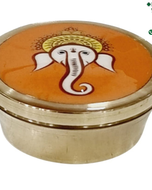 Ganesha Kumkum Box, small round brass box with a printed orange disc on the lid showing a white Ganesha face