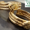 Impon Toe Ring, two gold-toned textured metal rings featuring a central faceted stone and a braided band detail resting on a dark surface