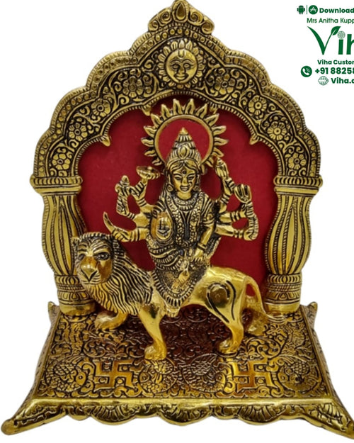 Durga in white metal, multi-armed figure on a lion within an ornate arch with a red backing panel