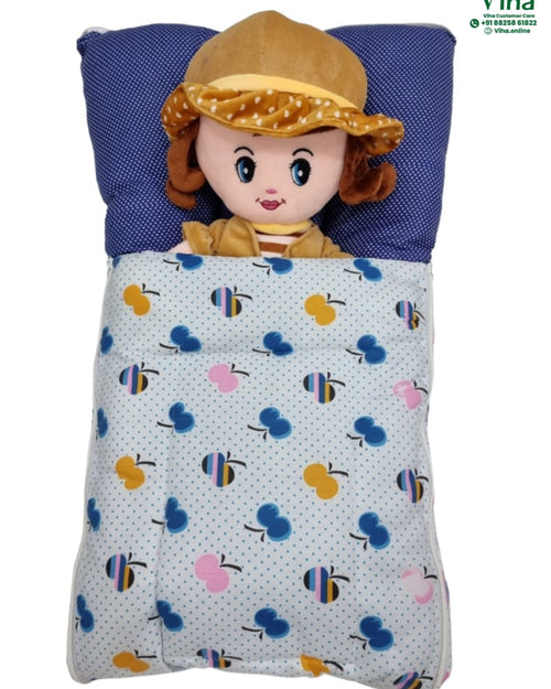 Baby Sleeping Bag, a doll in a yellow-toned hat lies on a blue polka-dot pillow, covered by a light-colored blanket patterned with blue, yellow and pink apples