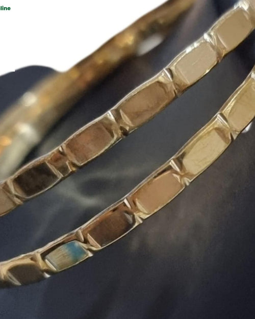 Impon Bangle, two gold-toned metallic bangles with a faceted, block-patterned outer surface and glossy finish resting on a dark surface
