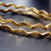 Impon Neli Bangle, two gold-toned wavy-edged bangles with textured ridges on the outer surface against a dark background
