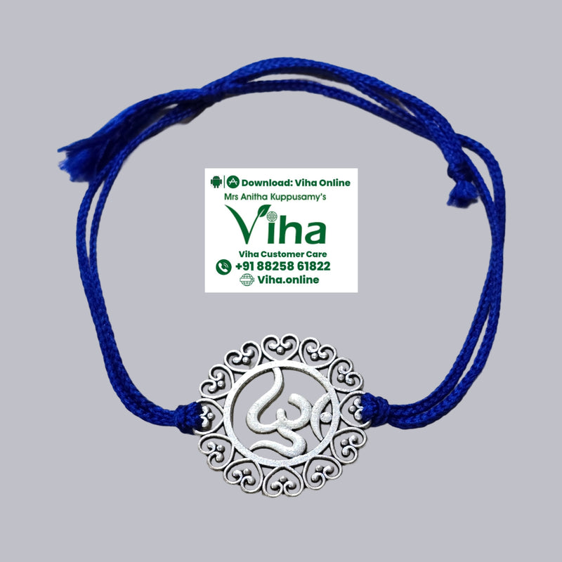 White Metal Rakhi, a grey-toned circular metal pendant with an ornate heart-cutout border and a central symbol, threaded onto a dark blue string