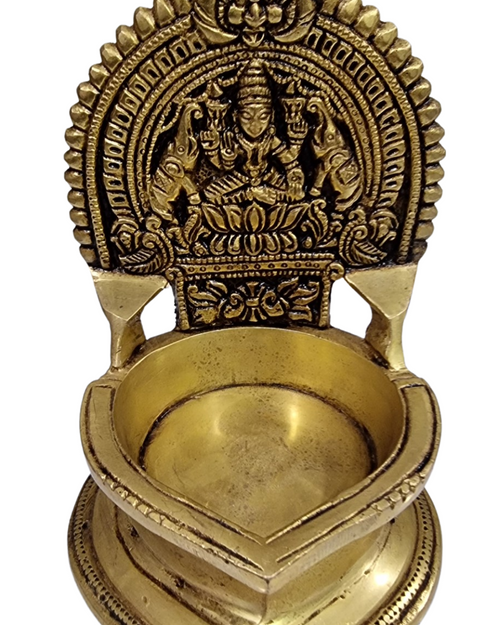 Antique brass Gajalakshmi vilakku, ornate Lakshmi arch above a teardrop oil bowl on a pointed foot