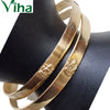 Impon Mahalakshmi Bangle, two gold-toned metal bangles with brushed surfaces and small embossed figure motifs displayed on a dark stand