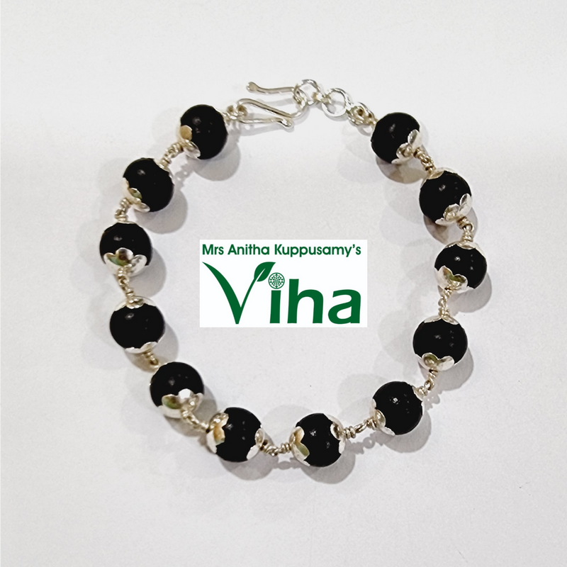 Karungali Bracelet Silver with Cappings, a bracelet with twelve black spheres and silver-toned metal caps linked by twisted wire on a white surface