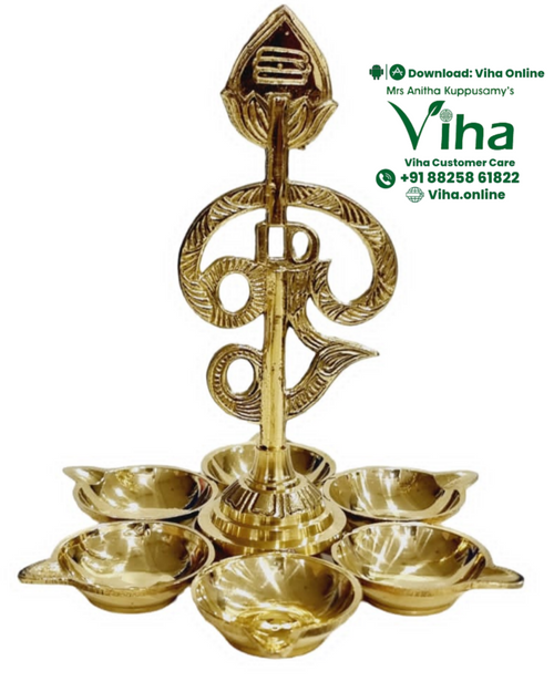 Arumuga Vel Lamp, a gold-toned metallic object featuring six small bowl-shaped dishes arranged in a circle around a central vertical stem with a finial
