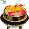 Jaladeepam Lamp, a gold-toned metallic bowl holding pink petals and yellow flower pieces with one lit yellow candle on a matching footed base