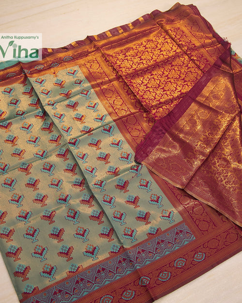 Soft Silk Saree With Blouse, a folded grey-green textile with red, blue and gold-toned patterns and a broad red-toned patterned border