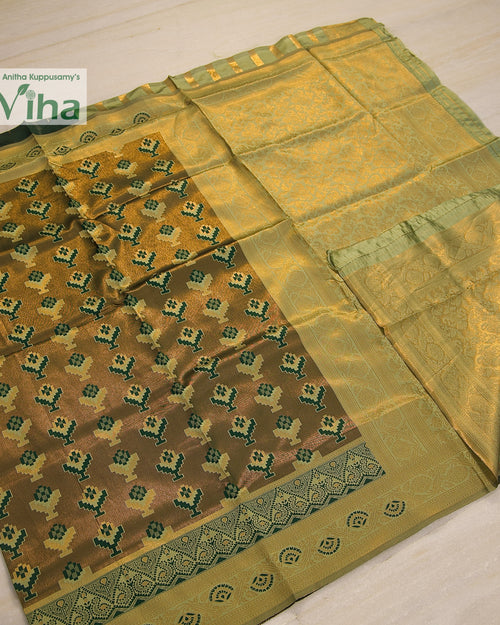 Soft Silk Saree With Blouse, a folded green fabric with a glossy finish featuring repeating patterned blocks and borders in gold-toned hues