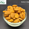 Almond, a clear glass bowl filled with numerous ribbed, brown teardrop-shaped seeds sits against a dark grey background