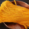 A bundle of bright yellow cotton lamp wick strands resting in a copper dish