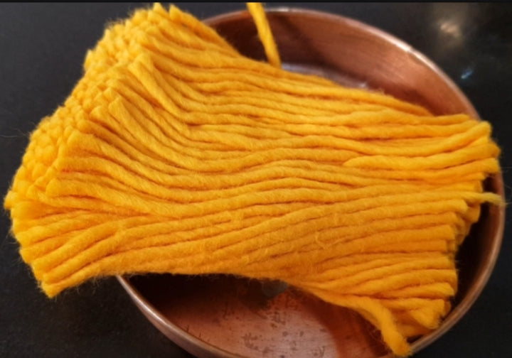 A bundle of bright yellow cotton lamp wick strands resting in a copper dish