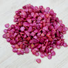 Annamalai Brinjal Seeds, a pile of small, flat, magenta-colored seeds with glossy surfaces is arranged on a light wood-grained surface