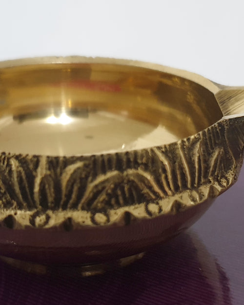 Agal Vilakku Brass Small, a gold-toned metal bowl with a glossy interior and a patterned outer band features one small protruding handle