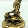 Krishna in brass, child figure seated on a round engraved base with one hand raised to the mouth