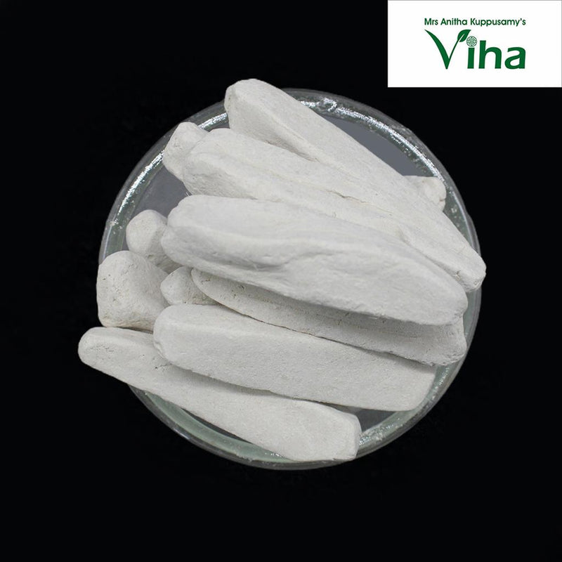 Namakatti, a pile of grey-white elongated chalk sticks and irregular stones in a clear glass dish against a black background
