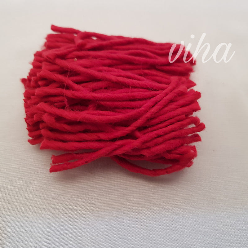 A folded bundle of red cotton lamp wick strands on a pale surface