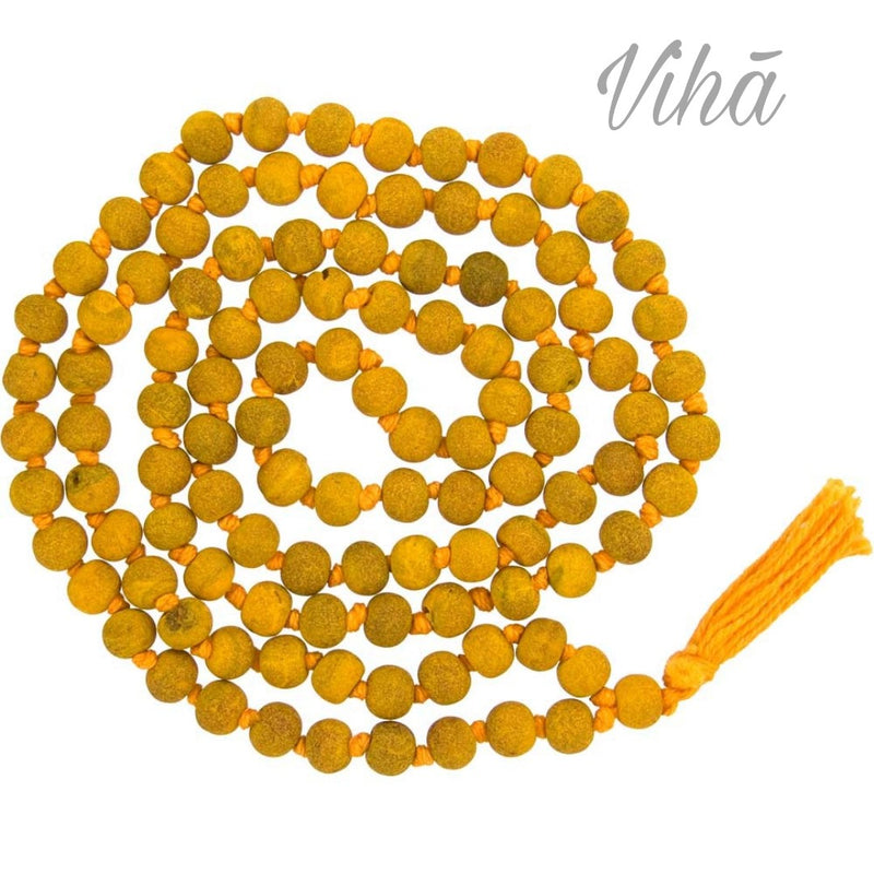 Haldi Mala / Turmeric Mala, a long strand of matte yellow beads, threaded and knotted together with orange string, terminating in an orange tassel