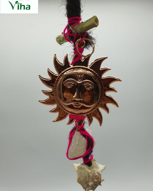 Kan Drishti Sun Face Hanger, copper sun-face medallion hanging from black hair wrapped in pink thread, with a conch shell