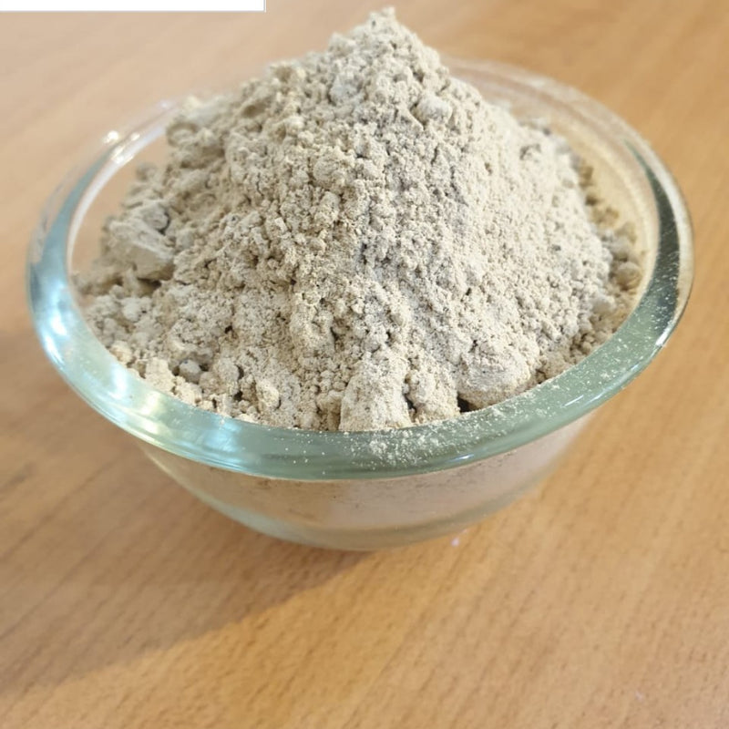 Ashwagandha Powder, a clear glass bowl filled with grayish powder sits on a wooden surface