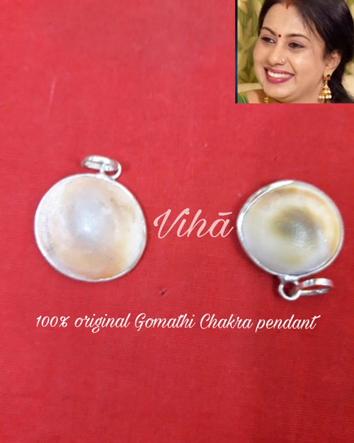 Gomathi Chakra Pendant, two round silver-toned metal pendants with domed white and brown inserts and top loops on red surface