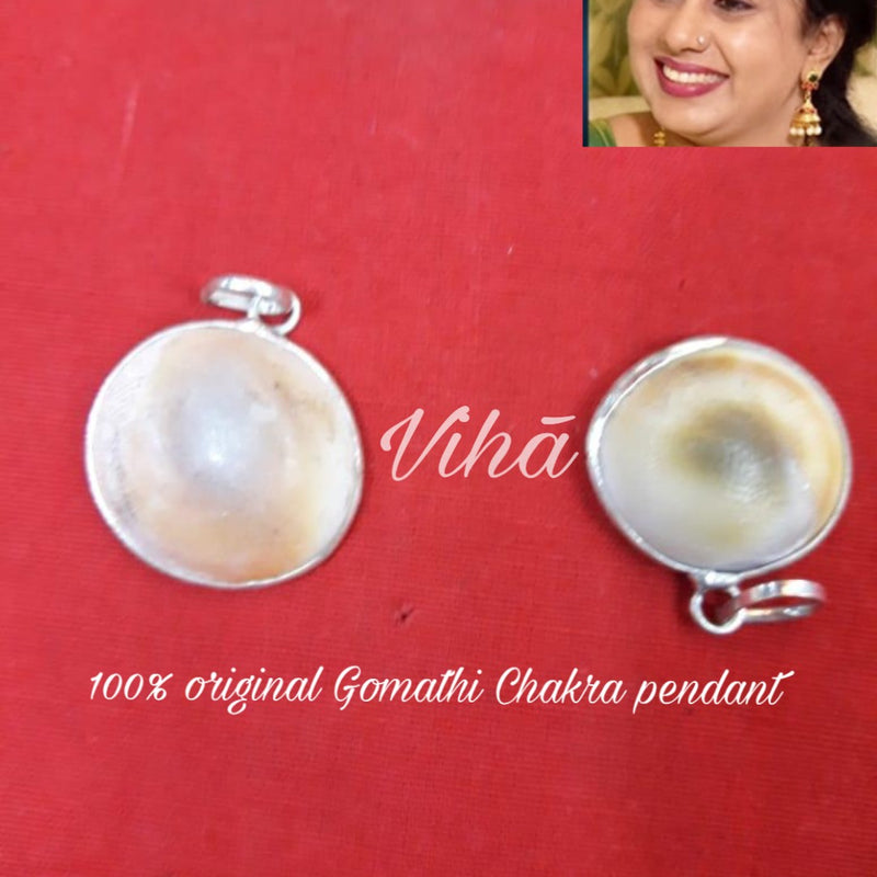 Gomathi Chakra Pendant, two round silver-toned metal pendants with domed white and brown inserts and top loops on red surface