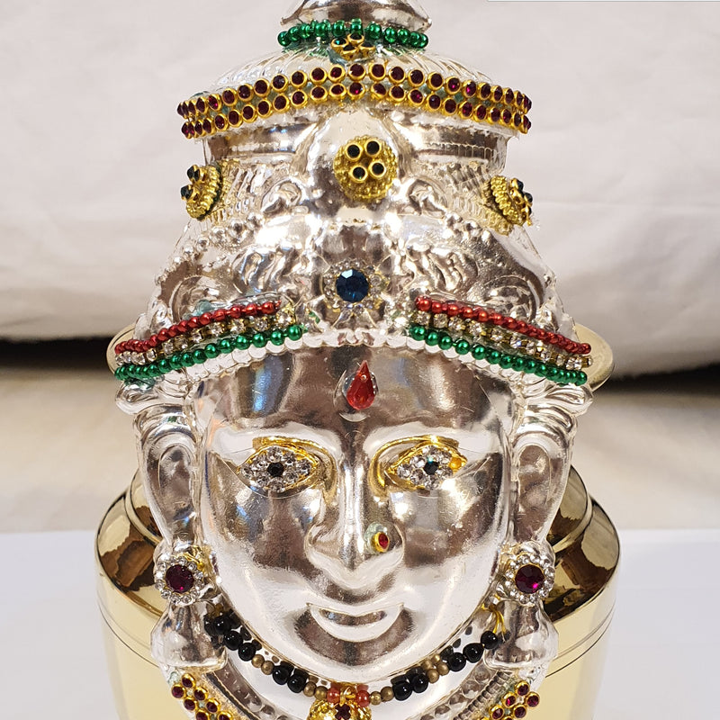 Amman Face Decorated With Jewels, a silver-toned face mask with gold-toned details, colored stones, and black beads on a gold-toned pot