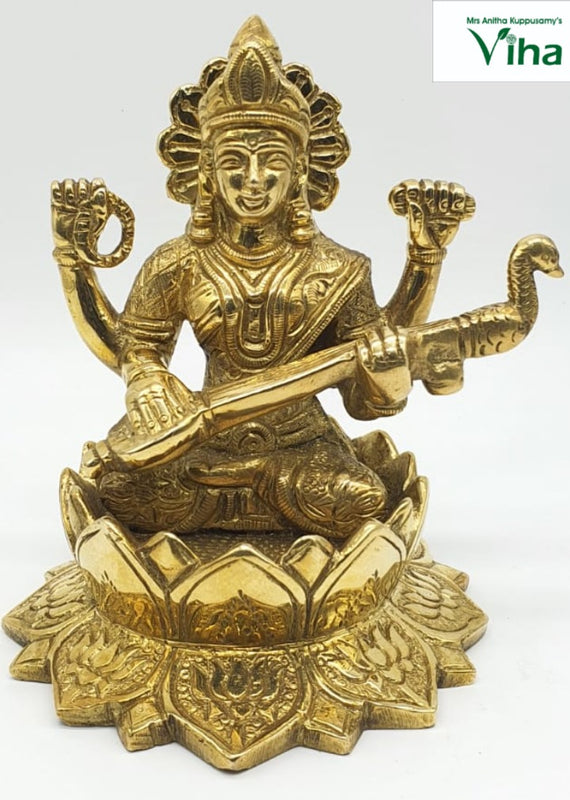 Saraswathi in brass, four-armed figure with a rayed halo seated on a wide lotus base with a veena and a peacock