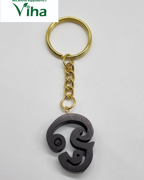 Karungali Tamil OM Keychain, a gold-toned metal split ring with a short chain suspends a dark brown Tamil letter pendant with a smooth surface