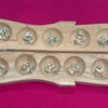 Pallanguzhi With Chozhi, a light brown wooden board with fourteen circular hollows containing small greyish white oval cowrie shells against a pink surface