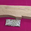 Pallanguzhi With Chozhi, a light brown wooden cutout board and a small clear plastic bag of many small white shells on a fuchsia cloth background