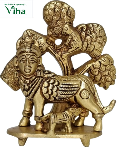 Kalpavriksha Kamadhenu in brass, human-faced cow with a calf beneath, against a carved tree with a peacock above