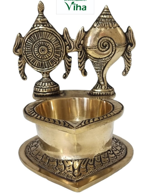 Sangu chakra vilakku in brass, conch and wheel discs standing behind a deep oil bowl on a heart-shaped base
