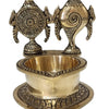 Sangu chakra vilakku in brass, conch and wheel discs standing behind a deep oil bowl on a heart-shaped base