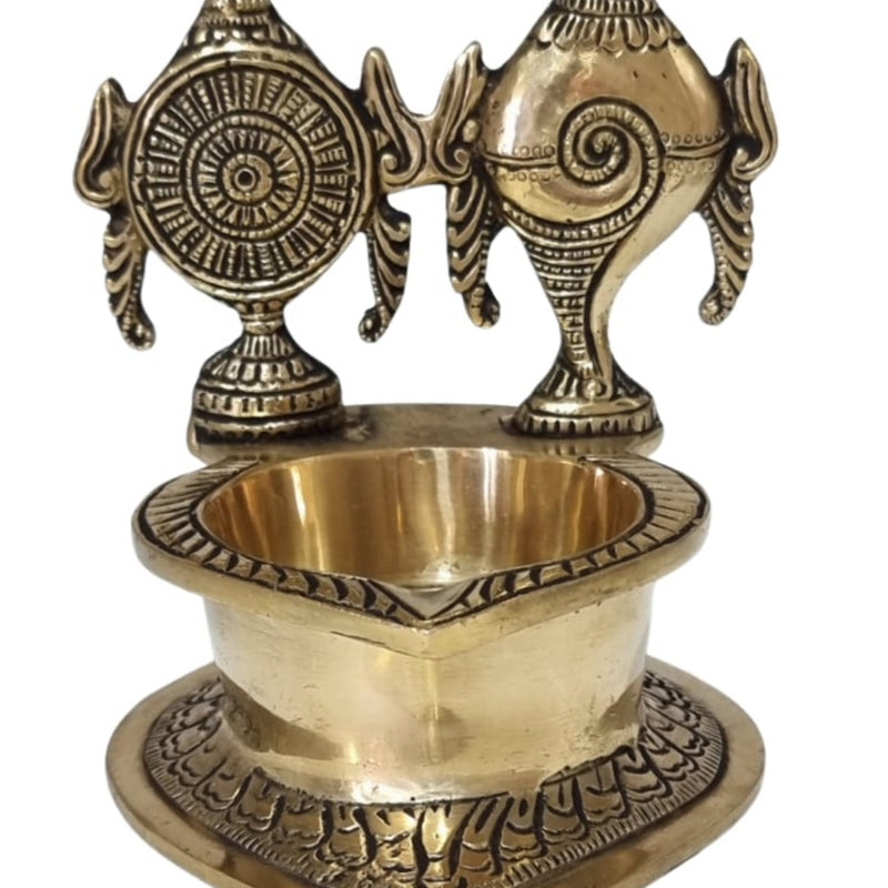 Sangu chakra vilakku in brass, conch and wheel discs standing behind a deep oil bowl on a heart-shaped base