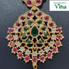 Impon Necklace, a gold-toned ornate pendant featuring pink and green stones, clear stones, and a hanging white bead, all set against a dark textured surface