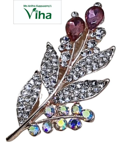 Saree Pin, a shiny gold-toned metallic leaf-shaped ornament with clear sparkly stones, two reddish-pink teardrop stones, and eight iridescent stones