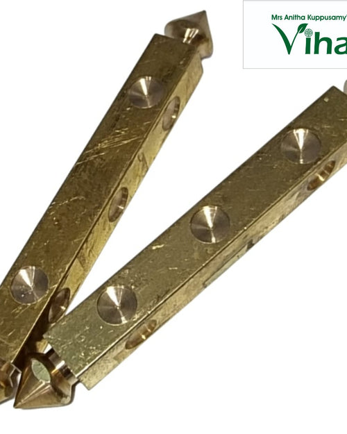 Dhayakattai Brass, two gold-toned metallic square-rod objects with four conical indentations and pointed tips on each end against a white background