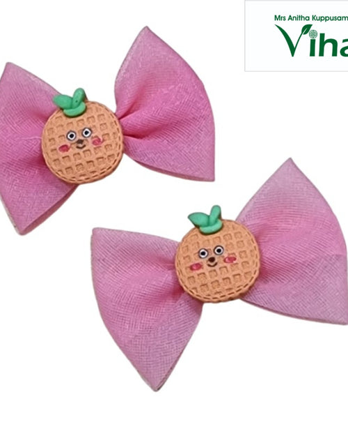Hair Clip Premium Quality, two pink fabric bows adorned with two waffle-patterned round orange charms with green stems and faces
