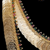 Impon Lakshmi Kasu Malai, gold-toned coin necklace and one matching earring adorned with red and green stones against a black background