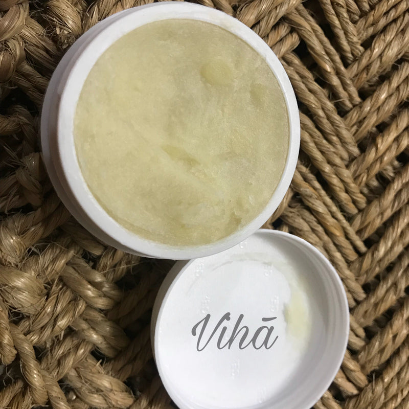 Shea Butter, an open circular white jar filled with pale yellow solid on a woven brown rope background with one detached white lid beside it