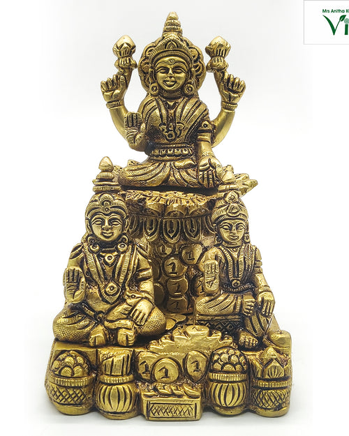 Kuberar in brass, a standing figure above two seated figures, with pots and coin heaps across the base